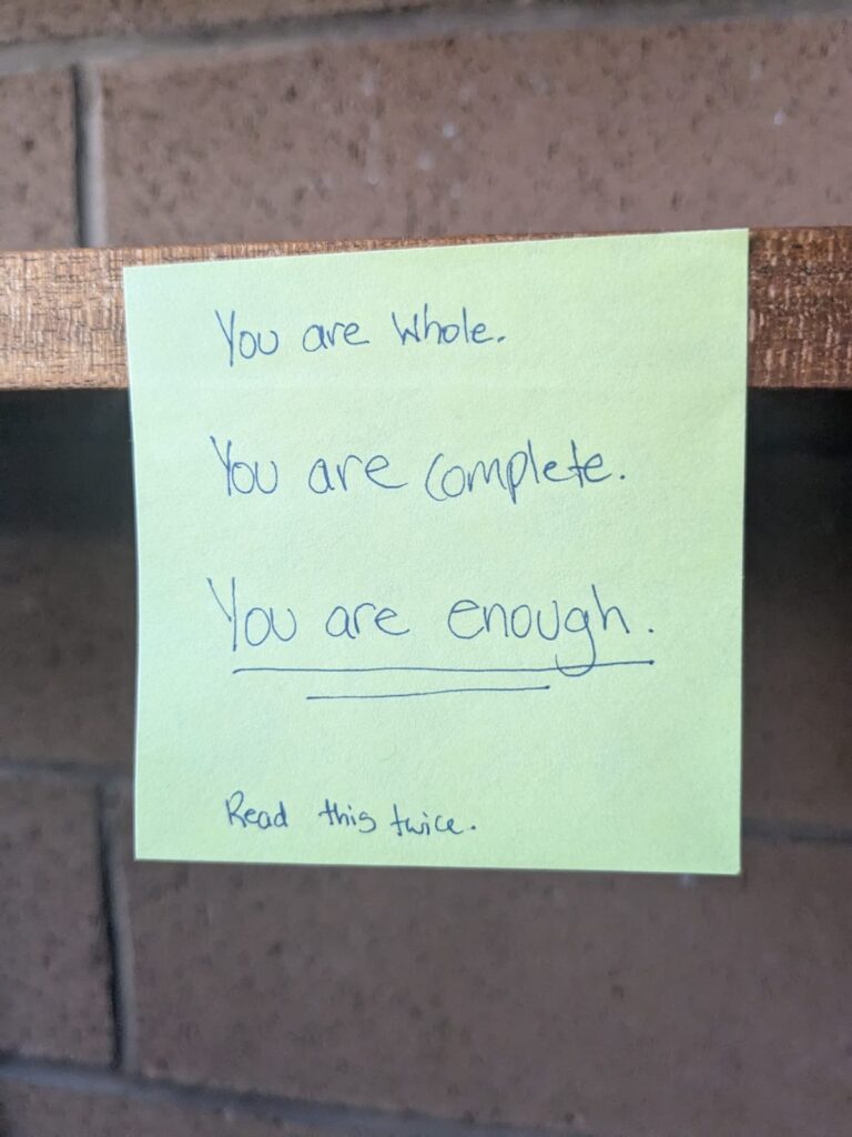 Sticky note stuck on a shelf with the words "You are whole. You are complete. You are enough." 
